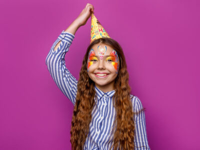 Birthday girl with colorful faceart wear party cap posing isolat